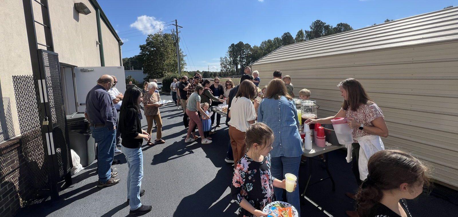 Church members carrying plates along the tables at an outdoor fellowship meal